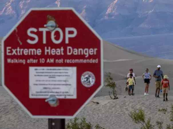 People walk among sand dunes near a sign warning of extreme heat danger in Death Valley National Park on Saturday. (Credit: David McNew/Getty Images)