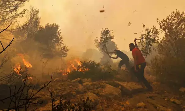 Residents help firefighters try to extinguish a wildfire burning near Athens, on 19 July 2023. (Credit: Miloš Bičanski/Getty Images)