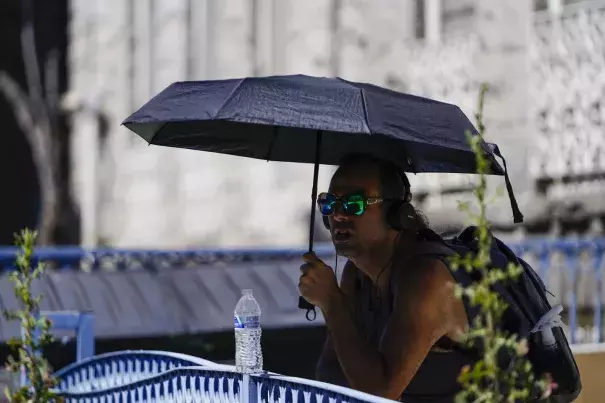 A man uses an umbrella to avoid the midday sun, Tuesday, July 11, 2023, in Los Angeles where highs may approach or exceed 100 degrees Fahrenheit this week. (Credit: AP Photo/Ryan Sun)