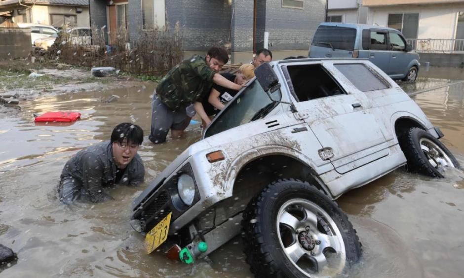 Residents try to upright a vehicle stuck in a flood hit area in Kurashiki, Okayama prefecture on July 9, 2018. Credit: CNN