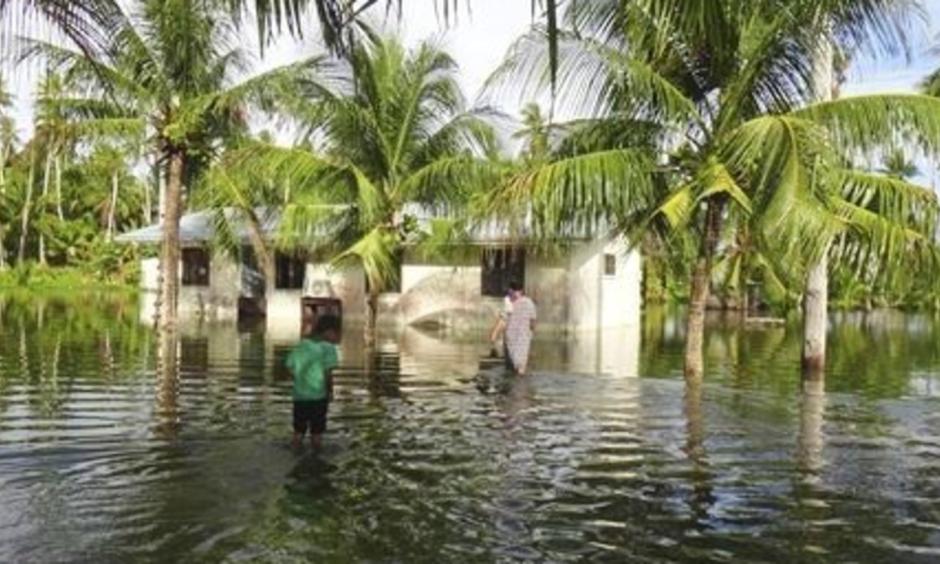 A woman and a child walk through knee-deep water to reach their home during a king tide event on Kili in the Marshall Islands in January 2015. Photo: Bikini Atoll Local Government / Associated Press