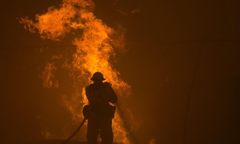 A firefighter hoses down burning pipes near a water tank. Photo: David McNew/Getty Images
