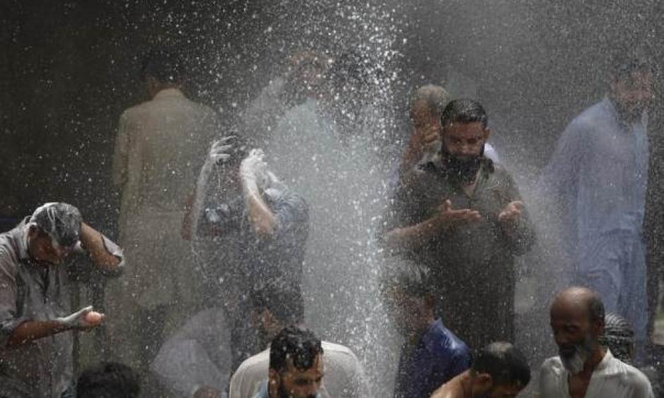 People are seen bathing while others cool off from the heat as they are sprayed with water jetting out from a leaking water pipeline in Karachi, Pakistan, June 25, 2015 during a heat wave. Photo: Akhtar Soomros, Reuters