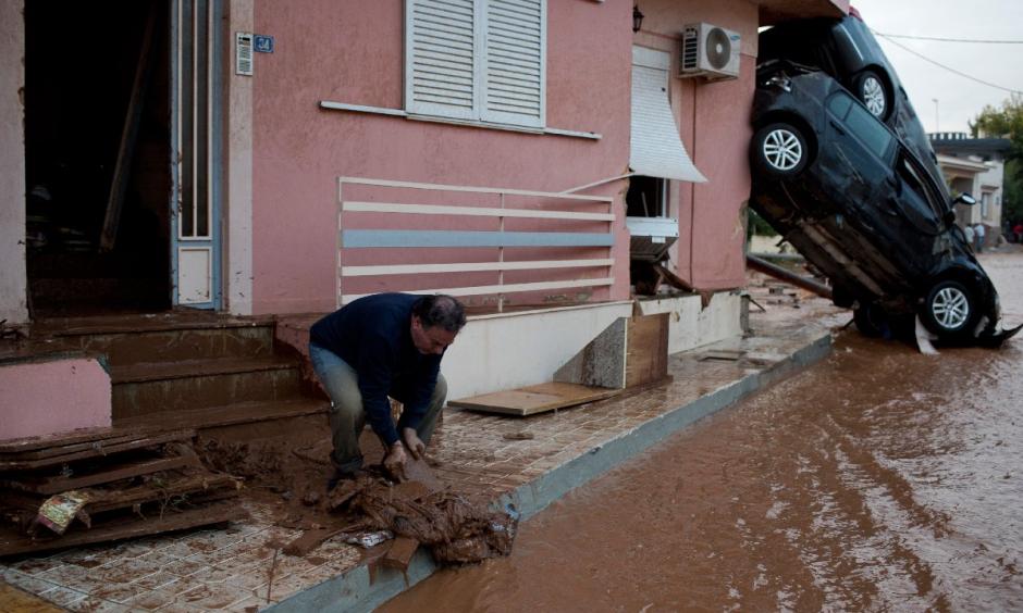 A man clears mud from his home in front of flipped over cars in the municipality of Mandra western Athens, on Wednesday, Nov. 15, 2017. Photo: Petros Giannakouris, AP