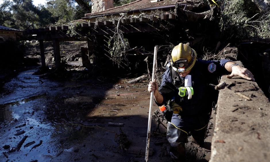 Alex Broumand of the Montecito Fire Department walks in mud in front of homes damaged from storms in Montecito, Calif. on Thursday. Rescue workers used long poles to probe knee-deep ooze for bodies Thursday. Photo: Marcio Jose Sanchez, AP