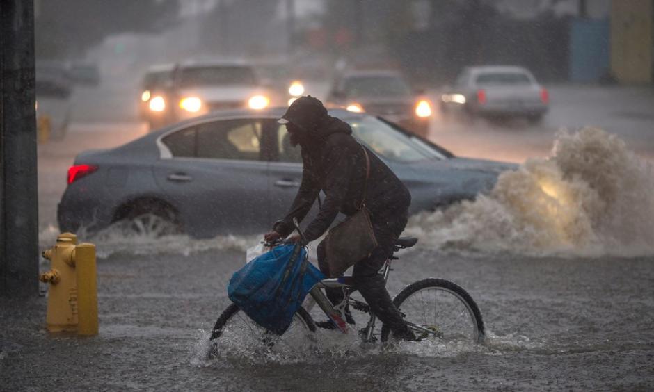 A bicyclist in Sun Valley rides along a flooded street as powerful atmospheric river storms move across California. Photo: David McNew, Getty Images