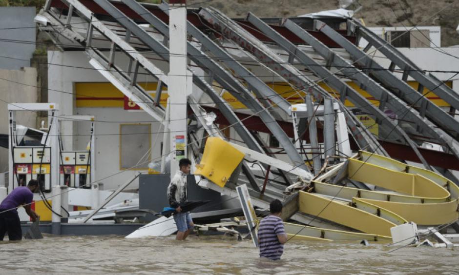 People walk next to a gas station Wednesday flooded and damaged by the impact of Hurricane Maria in Humacao, Puerto Rico. Photo: Carlos Giusti, AP