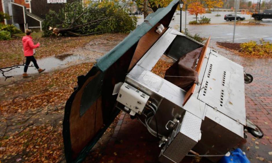 A woman walks by a food stand and a tree that were toppled by a storm in Freeport, Maine, Monday, Oct. 30, 2017. Photo: Robert F. Bukaty, AP