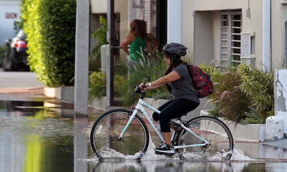 A young student on her bicycle carefully crosses the street on Lincoln Road Court in Miami Beach Thursday where the annual king tide caused flooding. Photo: C.M. Guerrero