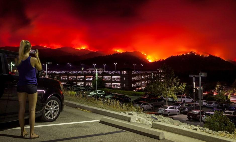 A woman takes photos from the upper parking lot of the Cache Creek Casino Resort overlooking the County fire as it burns out of control Saturday in Brooks, Calif. The blaze spread quickly overnight. Credit: Peter DaSilva, EPA, Shutterstock