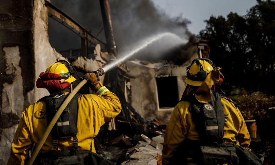 Humboldt County firefighters Bobby Gray, left, hoses down smoldering flames inside a destroyed home Marcus Yam, Los Angeles Times