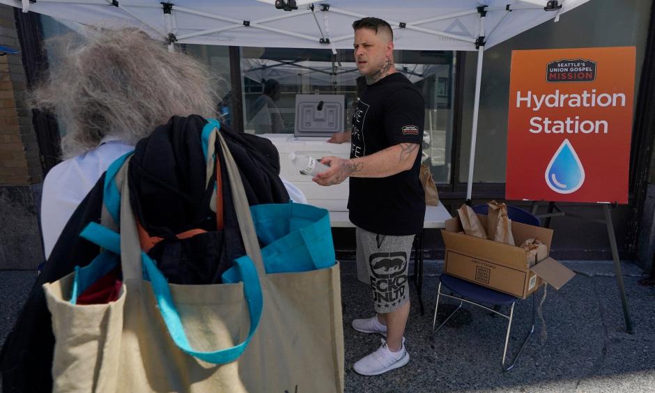 Carlos Ramos hands out bottles of water and sack lunches on Monday at a hydration station in front of the Union Gospel Mission in Seattle. (Ted S. Warren/Associated Press)
