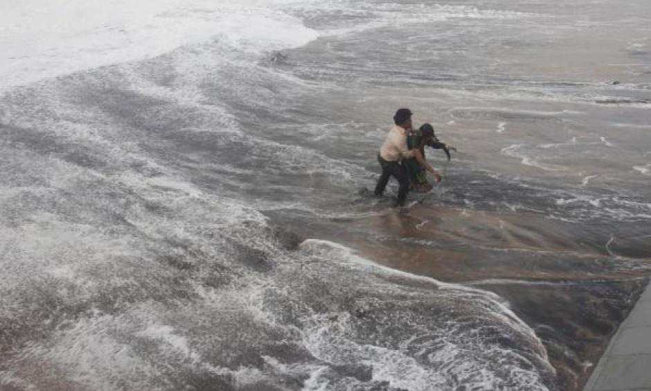 A man carries his wife to a safer ground after a wave hits a beach in Gopalpur in Ganjam district in the eastern Indian state of Odisha October 12, 2014. Image: Stringer, Reuters
