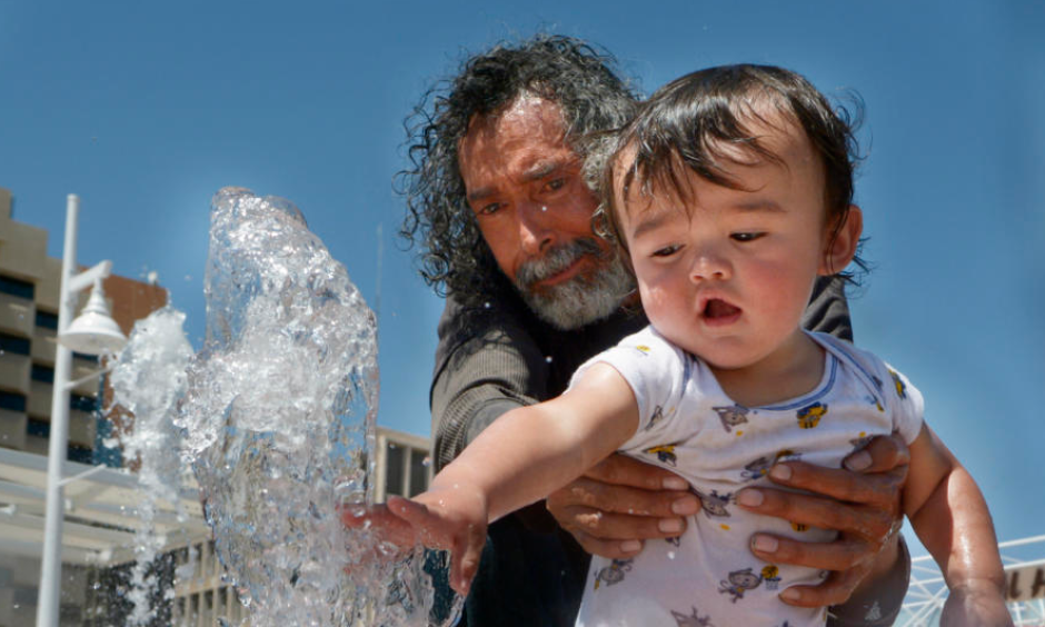 Ernest Espinosa and his grandson, Mariano Espinosa, 1, beat the heat by playing in the Civic Plaza fountain Monday. Albuquerque hit a record high of 98 degrees Monday, but temperatures will drop slightly this week as a cold front pushes into New Mexico. Credit: Greg Sorber, Albuquerque Journal