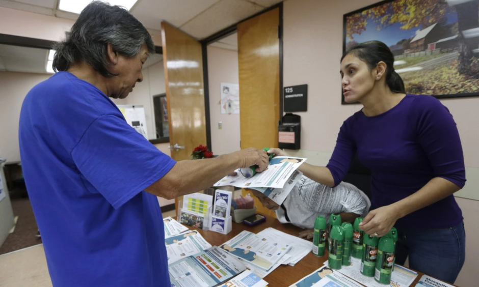 A worker at the Wynwood Community Service Center, right, hands a brochure and a can of insect repellent to a local resident in Miami-Dade County. Photo: Alan Diaz / AP