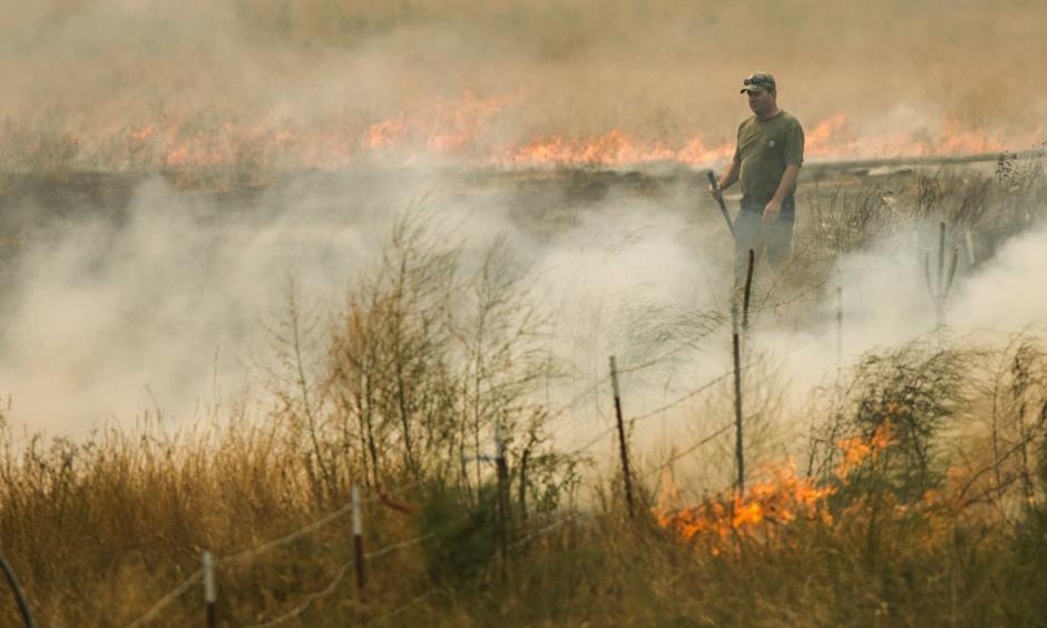 Ken Maple helps put out a grass fire that spread from a neighbor’s property northwest of Omak on Aug. 20. Photo: Bettina Hansen, The Seattle Times