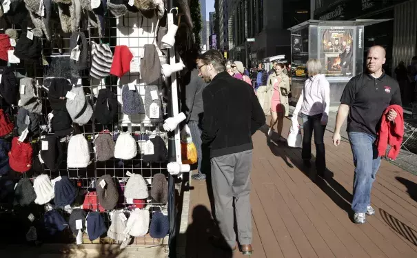 Pedestrians walk on the sidewalk past winter hats for sale in New York, on Dec. 15. Photographer: Mark Lennihan/AP Photo