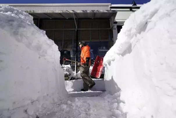 Bradley Winn, of Cohasset, Mass., carries a snow shovel past a snow bank on a sidewalk, Sunday, Jan. 30, 2022, in Scituate, Mass. Gusty winds and falling temperatures plunged the East Coast into a deep freeze as people dig out from a powerful nor’easter that dumped mounds of snow, flooded coastlines and knocked power out. (AP Photo/Steven Senne)