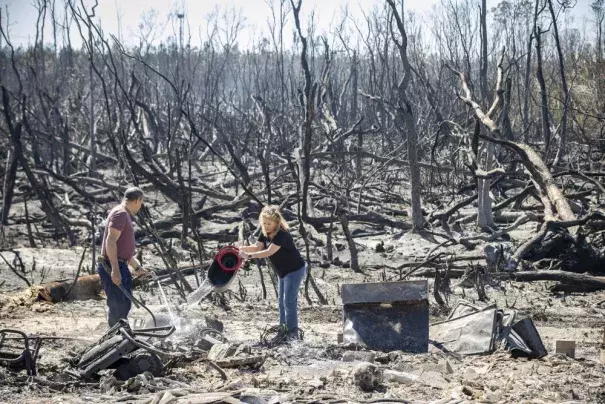 Hector Rivera and Wandi Blanco put water on hotspots behind their home in Panama City, Fla., Saturday, March 5, 2022, following a wildfire that started Friday. The fire destroyed two homes next to them and melted the siding off of their home. (Credit: Mike Fender/News Herald via AP)