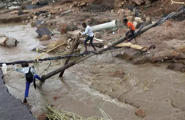 People walk across a makeshift bridge over a river, after a bridge was swept away in Ntuzuma, outside Durban, South Africa, Tuesday, April 12, 2022. Prolonged rains and flooding in South Africa's KwaZulu-Natal province have claimed the lives of at least 20 people, according to local officials. (Credit: AP Photo/Str)