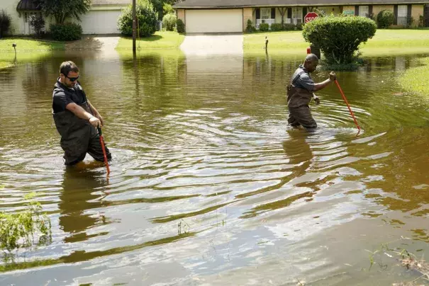 Hinds County Emergency Management Operations deputy director Tracy Funches, right, and operations coordinator Luke Chennault, wade through flood waters in northeast Jackson, Miss., Monday, Aug. 29, 2022, as they check water levels. Flooding affected a number neighborhoods that are near the Pearl River. (Credit: AP Photo/Rogelio V. Solis)