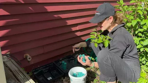 Ava Dickman, a technician with AAA Exterminating Inc., refills rodenticide in a bait station to exterminate mice and rats outside a home in Indianapolis, Monday, May 16, 2022. Scientists say climate change is likely contributing to a rodent boom that is making more work for pest control experts. (Credit: AP Photo/Casey Smith)