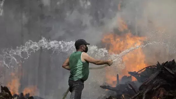 A local resident uses a garden hose to try to stop a forest fire from reaching houses in the village of Figueiras, outside Leiria, central Portugal, Tuesday, July 12, 2022. Hundreds of firefighters in Portugal continue to battle fires in the center of the country that forced the evacuation of dozens of people from their homes mostly in villages around Santarem, Leiria and Pombal. (Credit: AP Photo/Joao Henriques)