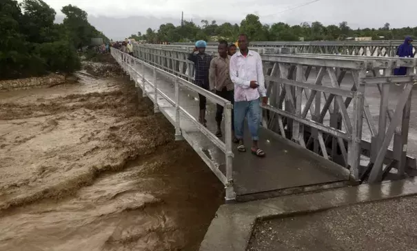 Floodwaters from Hurricane Matthew rage down a river as people cross a bridge in Port-au-Prince, Haiti. Photo: Carlos Garcia Rawlins, Reuters