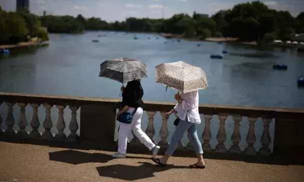 People use umbrellas to shelter from the sun in Hyde Park, London, on Saturday. (Photograph Credit: Henry Nicholls/Reuters)