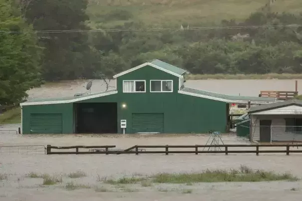 A person speaks on their phone as they look out of their window at the flood waters surrounding their property in Huapai, north-west of Auckland, on Tuesday. (Credit: Phil Walter/Getty Images)