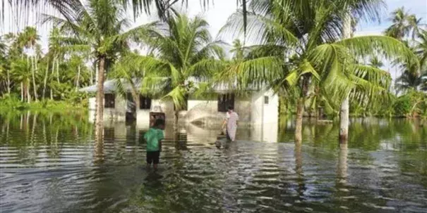 A woman and a child walk through knee-deep water to reach their home during a king tide event on Kili in the Marshall Islands in January 2015. Photo: Bikini Atoll Local Government / Associated Press