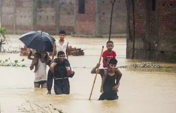 Nepalese men carry children on their shoulders as they wade through flood waters in village Ramgadhwa in Birgunj, Nepal, Sunday, Aug. 13, 2017. Photo: Manish Paudel, AP