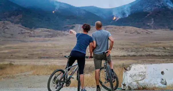 Two cyclists stopped to look at the Tenaja fire smoldering in the hills Thursday morning in Murrieta. A fast-moving fire erupted in hillside terrain near Murrieta on Wednesday night, quickly scorching almost 1,000 acres and prompting mandatory evacuation orders for multiple residential enclaves. Photo: Irfan Khan, LA Times