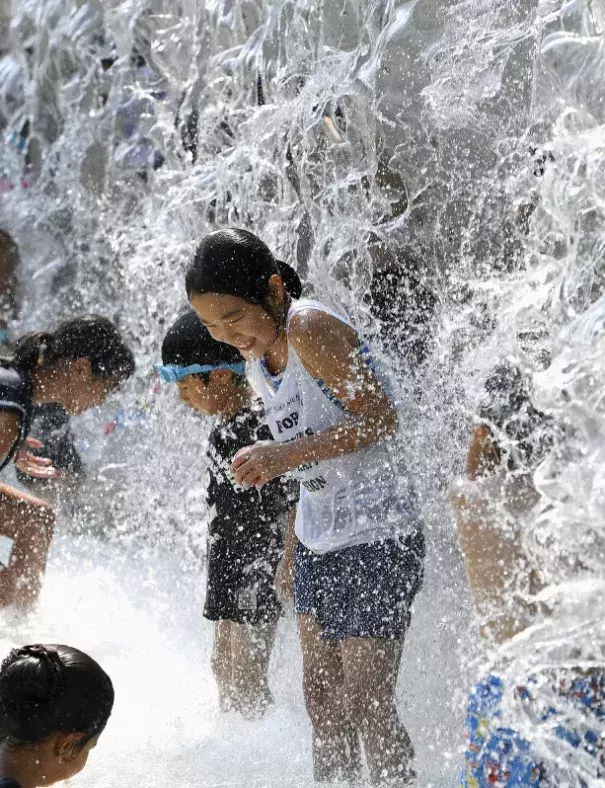 In this July 14, 2018 file photo, children play in a water fountain set up at a park in Tokyo during an extreme heat wave. (Kyodo)