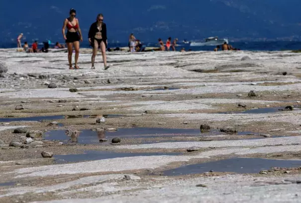 People walk as underwater rocks emerge from the water of Lake Garda after northern Italy experienced the worst drought in 70 years in Sirmione, Italy, August 16, 2022. (Credit: REUTERS/Flavio Lo Scalzo/File Photo)