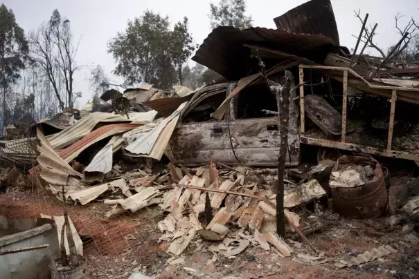 Charred remains of a home burned in a wildfire sit in a pile in Tome, Chile, Saturday, Feb. 4, 2023. Forest fires are spreading in southern and central Chile, triggering evacuations and the declaration of a state of a state of catastrophe on La Araucania region. (Credit: AP Photo/Matias Delacroix)