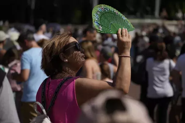 FILE - A tourist uses a fan to shade her face from the sun while waiting to watch the Changing of the Guard ceremony outside Buckingham Palace, during hot weather in London, July 18, 2022. (Credit: AP Photo/Matt Dunham, File)