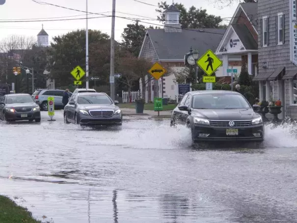 This Oct. 11, 2019, photo shows cars kicking up spray while driving through a flooded street in Bay Head, N.J. Bay Head is studying options to prevent, or at least reduce, incidents of so-called “sunny day” flooding caused by tides and rising sea levels, as well as major storm-related floods. New Jersey's Department of Environmental Protection and the U.S. Army Corps of Engineers have proposed a massive $16 billion plan to address back bay flooding along the shore. (AP Photo/Wayne Parry)