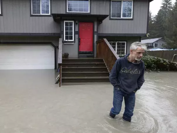 Bernie Crouse wades through water outside his home after the nearby South Fork Stillaguamish River crested early in the morning flooding several houses in this neighborhood, Dec. 5, 2023, in the Arlington area of Seattle, Washington. (Credit: Ken Lambert/AP)