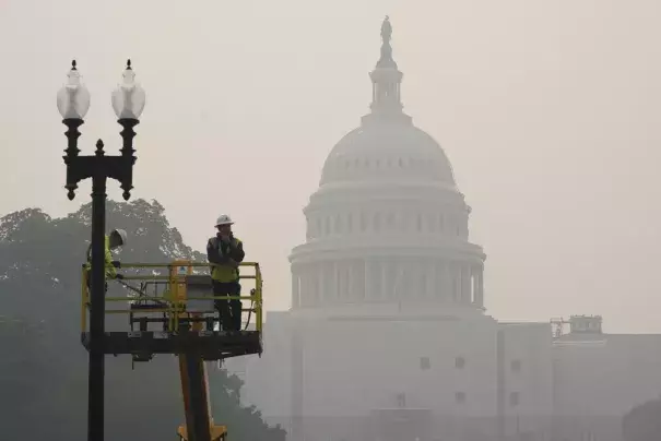 Workers finish tending a street lamp as smoke from Canadian wildfires obscures the view of the U.S. Capitol Building in Washington, Thursday, June 8, 2023. The haze from the wildfires is taking its toll on outdoor workers along the Eastern U.S. who carried on with their jobs even as dystopian orange skies forced the cancelation of sports events, school field trips and Broadway plays. (Credit: AP Photo/Susan Walsh)