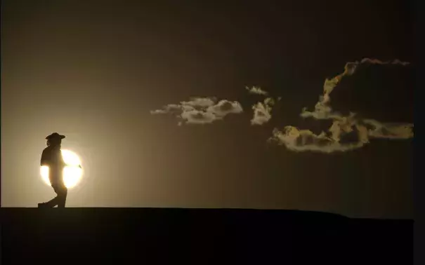 A person is shown walking on a trail at sunset
