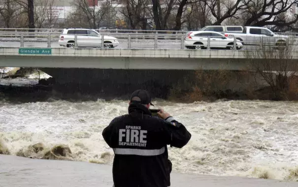 A firefighter from Sparks, NV, takes a picture of the rising Truckee River on Sunday, January 8, 2017, where it runs near the Grand Sierra hotel-casino along a line that divides the cities of Reno and Sparks. Photo: Scott Sonner, AP