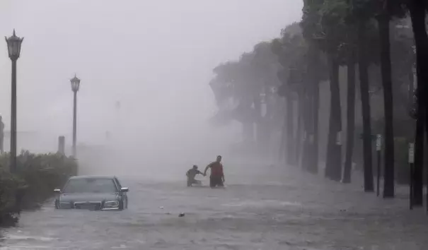 Pedestrians walk by a flooded car on a street as storm surge associated with Tropical Storm Irma hits Charleston, S.C., Monday, Sept. 11, 2017. Photo: Mic Smith, AP