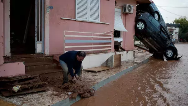 A man clears mud from his home in front of flipped over cars in the municipality of Mandra western Athens, on Wednesday, Nov. 15, 2017. Photo: Petros Giannakouris, AP