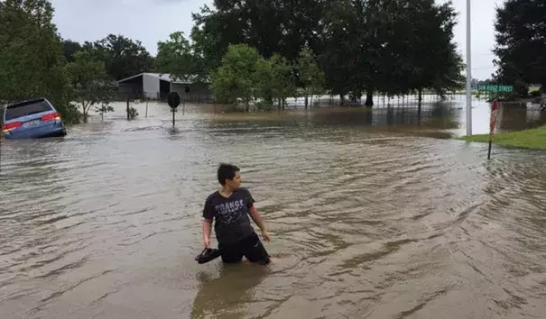 A person wades in floodwaters as a van is overtaken by water in a Youngsville, Louisiana neighborhood on Sunday, July 14, 2019, during Tropical Storm Barry. Credit: Mark Hargrave