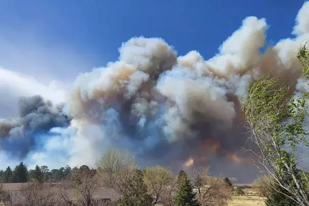 Smoke from a wind-whipped wildfire rises above neighborhoods on the outskirts of Flagstaff, Ariz., on Tuesday, April 19, 2022. Homes on the outskirts of Flagstaff were being evacuated Tuesday as high winds whipped a wildfire, shut down a major highway and grounded firefighting aircraft. (Credit: Sean Golightly/Arizona Daily Sun via AP)