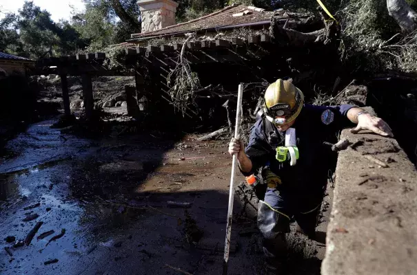 Alex Broumand of the Montecito Fire Department walks in mud in front of homes damaged from storms in Montecito, Calif. on Thursday. Rescue workers used long poles to probe knee-deep ooze for bodies Thursday. Photo: Marcio Jose Sanchez, AP