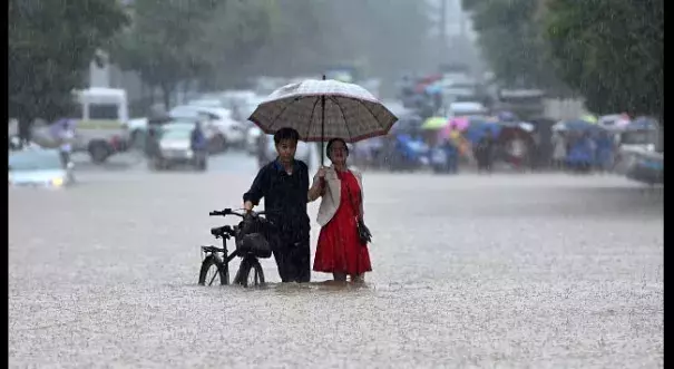 In this Wednesday, July 6, 2016 photo, a couple holding an umbrella in a rain wade through a flooded road in Wuhan in central China's Hubei province. Photo: Chinatopix via AP