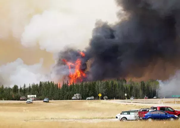 A convoy of evacuees drives south as flames and smoke rise along the highway near Fort McMurray, Alberta, on May 6. Photo: Getty Images