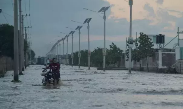 Men walk holding a motorcycle in a partially flooded street by the rains during this afternoon, in the Haitian capital Port-au-Prince, on May 2, 2017. Photo: Hector Retamal, Weather Underground via AFP/Getty Images